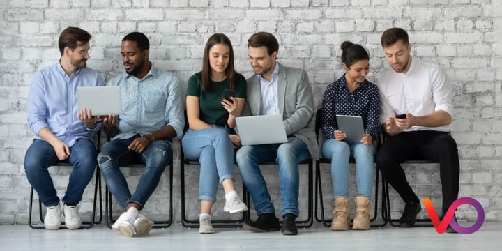 Six people seated in a row against a white brick wall, each using a different connected device including laptops, a tablet, and smartphones, illustrating multi-device streaming consumption. Viaccess-Orca logo bottom right.